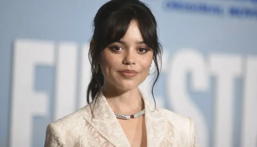 Jenna Ortega, uśmiechnięta, w białej koronkowej marynarce i efektownej biżuterii. Czy Jenna Ortega żyje? Tak, wygląda świetnie!