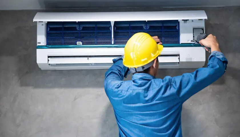 Técnico con casco amarillo trabajando en un aire acondicionado para quitar pitido.