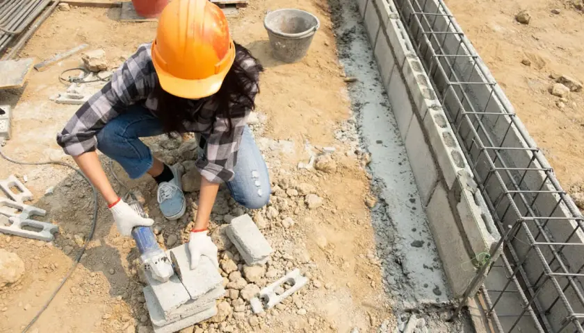 Budowlaniec w kasku obrabia bloczki betonowe, przygotowując je do budowy fundamentów z betonu c12/15.