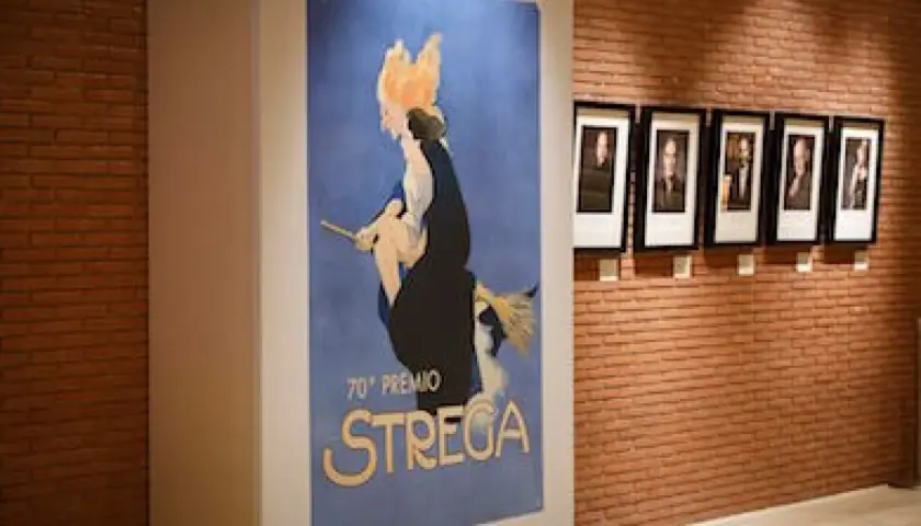 Un poster vintage celebra il 70° Premio Strega, con ritratti di autori appesi su una parete di mattoni.