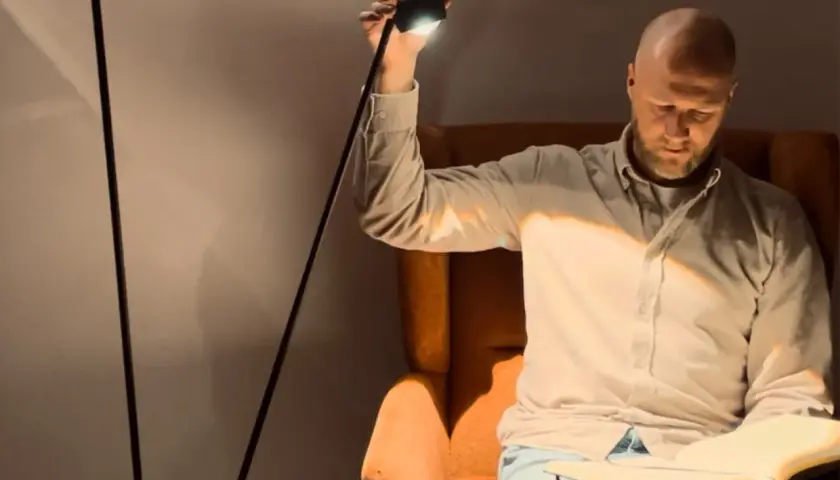 Hombre calvo sentado en sillón leyendo, iluminado por lámparas pie lectura.
