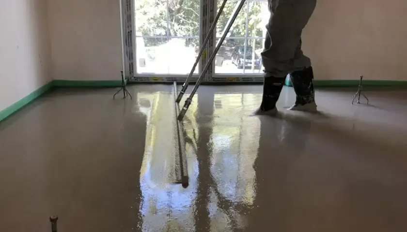 Pracownik wylewa beton, wyrównując go łaty. To kluczowe dla obliczenia, ile potrzeba cementu na 1m2 wylewki.