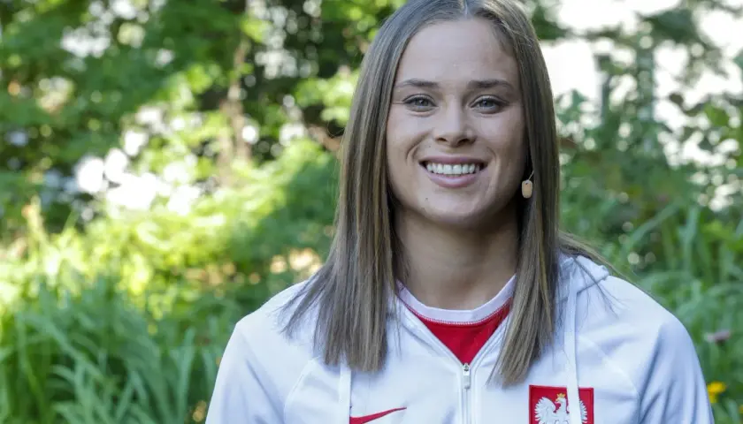 Uśmiechnięta Ewa Pajor, polska piłkarka, w białej bluzie z godłem Polski.
