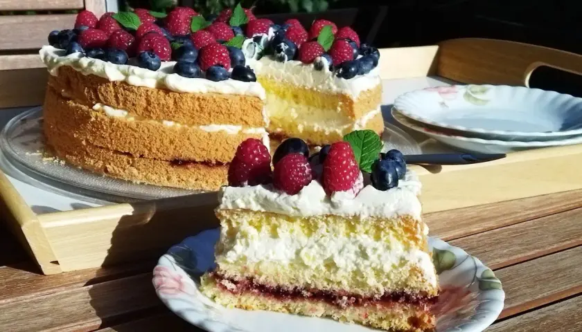 Tort biszkoptowy z kremem, malinami i borówkami, udekorowany miętą.