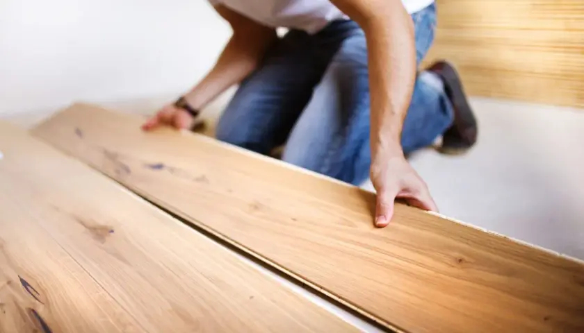 Uomo in ginocchio posa assi di legno per un pavimento con schema a spina di pesce.