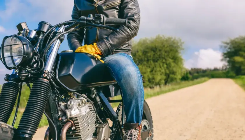 Motociclista con chaqueta de cuero y guantes amarillos, listo para la aventura. ¿Dyneema vs Kevlar? ¡La carretera espera!