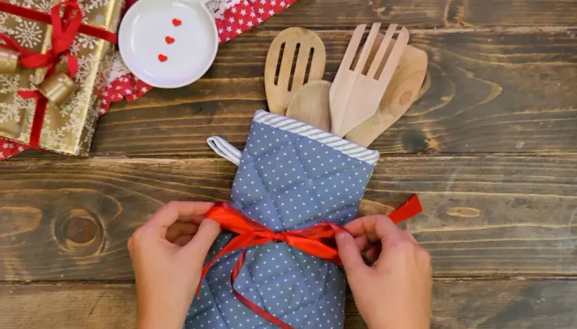 Idee regalo fai da te: un set di utensili da cucina in legno, avvolto in un guanto da forno a pois e legato con un nastro rosso.