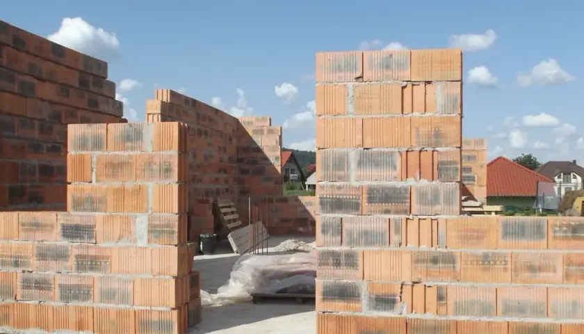 Budowa domu z pustaków ceramicznych. Widać ściany wznoszone z cegieł, które mają różne wymiary, tworząc konstrukcję.