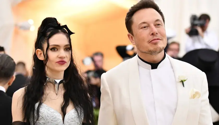 Grimes i Elon Musk na czerwonym dywanie. Ona w srebrnej kreacji z nietypowym naszyjnikiem, on w białej marynarce.