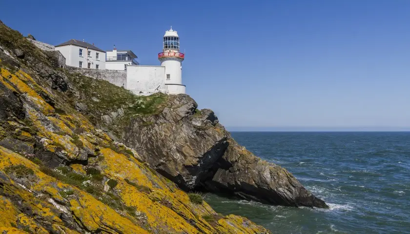 Biała latarnia morska na skalistym klifie nad morzem, Irlandia.