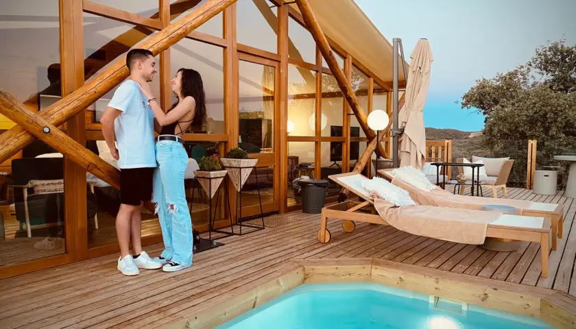 Pareja disfrutando de la tranquilidad de la dehesa experiences, con piscina y tumbonas en una cabaña de madera.