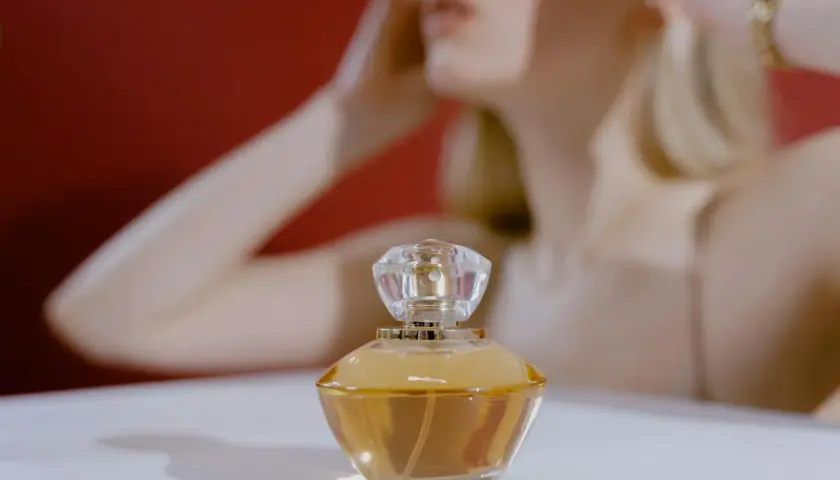 Elegancka buteleczka perfum z płynem o barwie **citral** na białym tle, w tle niewyraźna sylwetka kobiety.
