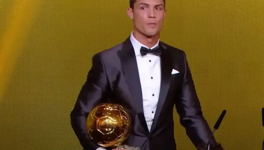 Cristiano Ronaldo w garniturze trzyma złotą piłkę. Ile złotych piłek ma Ronaldo? To pytanie zadaje sobie wielu fanów.