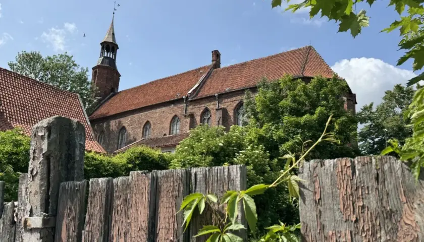 Stary, drewniany płot i ceglany kościół z wieżą w malowniczym mieście na Kociewiu.