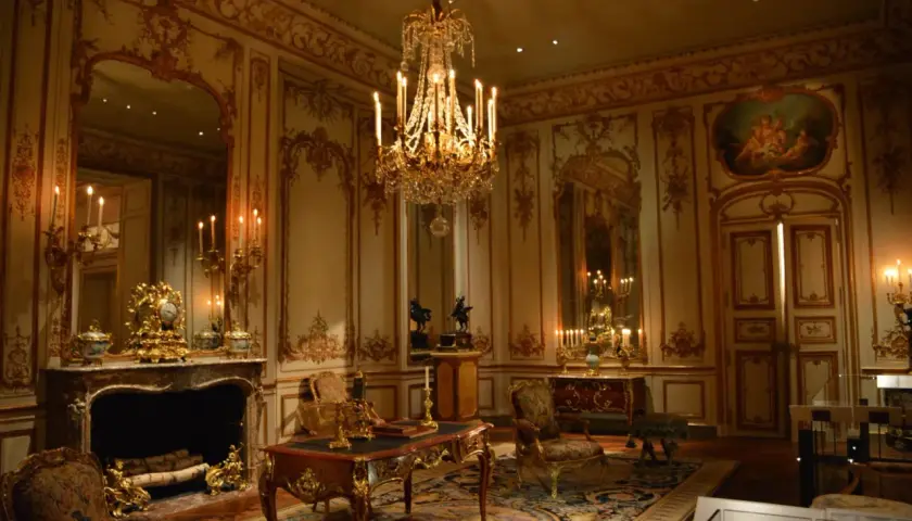 A lavish room with a crystal chandelier, ornate gold trim, and antique furniture embodies the royalcore aesthetic.