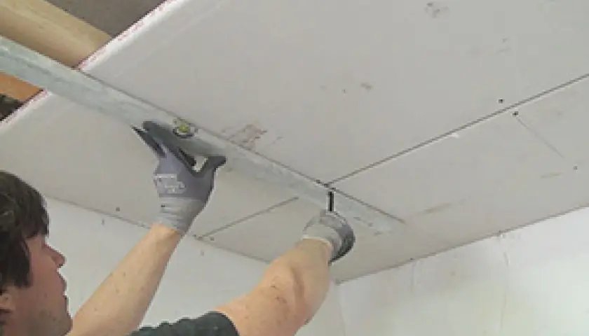 Handwerker bearbeitet Decke mit Rigipsplatten. Die Dicke der Platten ist entscheidend für Stabilität und Dämmung.