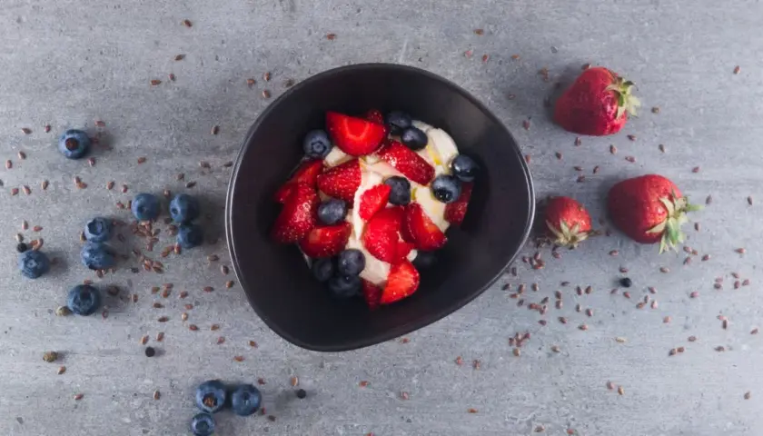 Schüssel mit cremigem low carb Joghurt, garniert mit frischen Erdbeeren und Blaubeeren. Leinsamen verstreut.
