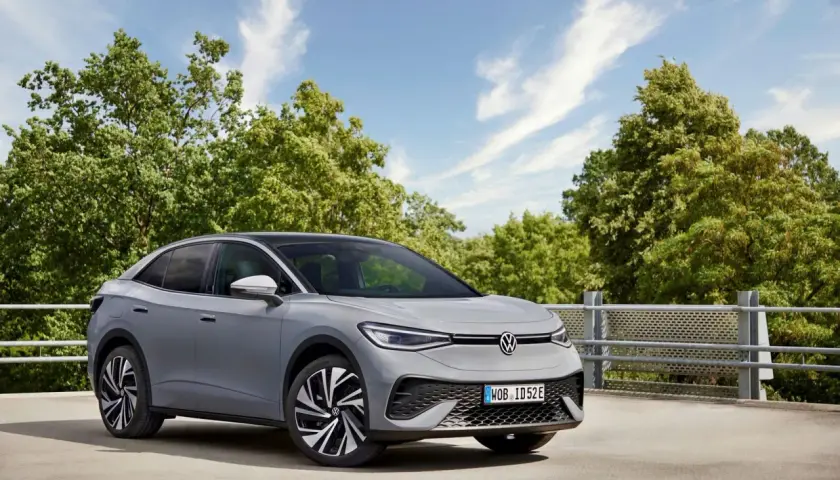 Szary VW ID.5 z czarnym dachem stoi na tle zielonych drzew i błękitnego nieba.