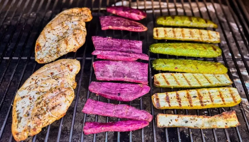 Deux blancs de poulet au barbecue, accompagnés de tranches de patate douce violette et de courgettes grillées, sur une grille.