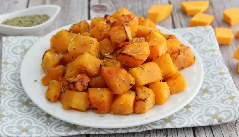 Zucca in friggitrice ad aria, dorata e profumata, servita su un piatto bianco con erbe aromatiche.