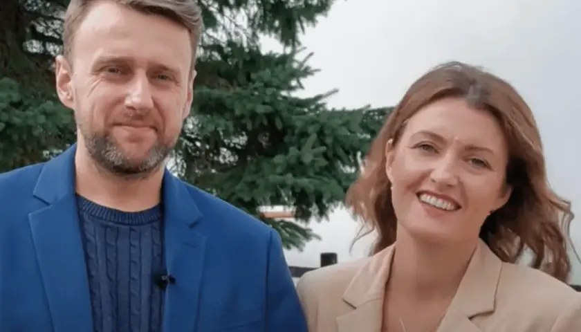 Uśmiechnięta para, on w niebieskiej marynarce, ona – żona z Ukrainy – w beżowej.