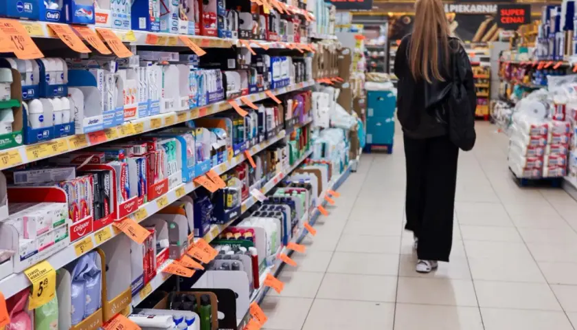 Kobieta spaceruje między regałami pełnymi produktów w sklepach w Czechach. Widać pasty do zębów, kosmetyki i inne artykuły.