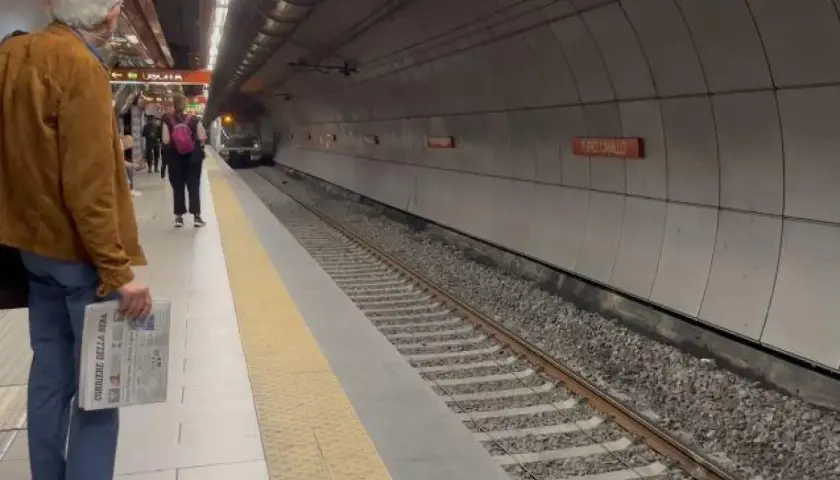 Uomo attende treno alla stazione Valle Aurelia Termini, con giornale in mano.