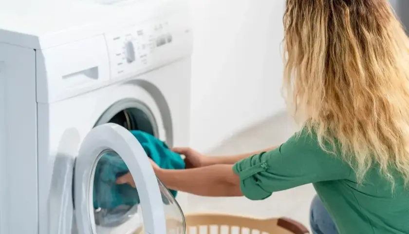 Kobieta wkłada pranie do pralki, która nie pobiera wody. Zmartwiona próbuje rozwiązać problem.