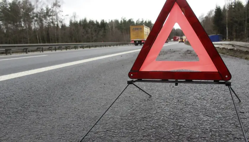 Trójkąt ostrzegawczy na poboczu drogi, zapowiadający 3 mieczy pozytywnie. W tle ciężarówka i inne pojazdy.
