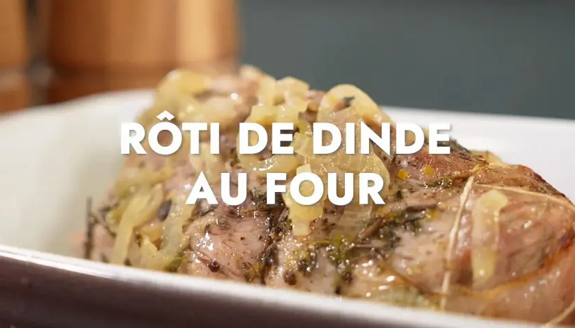 Un rôti de dinde au four, savamment assaisonné d'herbes et d'oignons, cuit à la perfection dans un plat en céramique.
