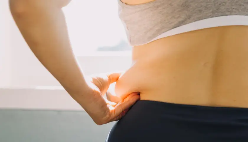 Dłoń chwyta fałd skóry na boku, symbolizując troskę o sylwetkę i chęć poznania, jak przyspieszyć metabolizm.