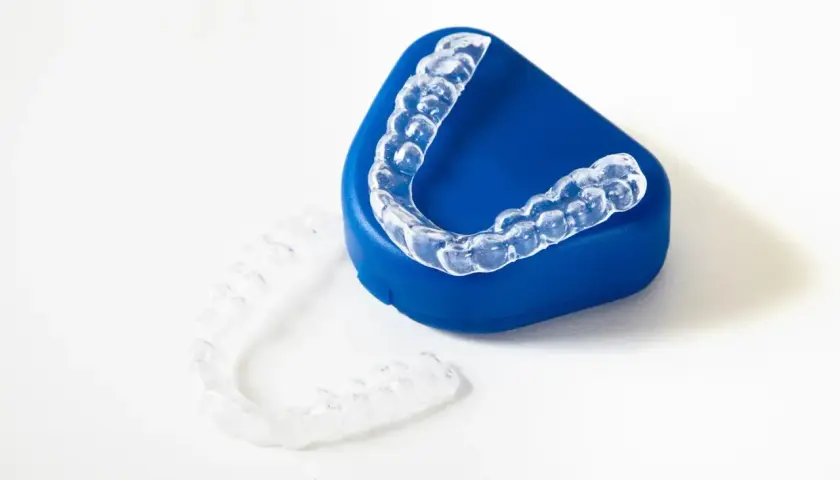 Alineadores transparentes para ortodoncia, uno sobre un estuche azul y otro al lado. ¿Cuánto cuesta el invisible line?