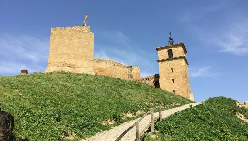 El castillo de San Vicente de la Barquera se alza majestuoso sobre una colina verde, con su torre y murallas de piedra bajo un cielo azul.