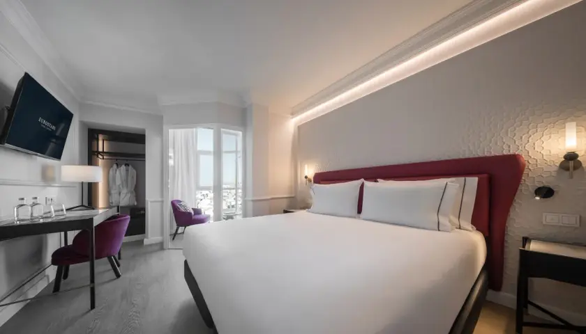 Habitación moderna y luminosa en el hotel San Antón Granada. Cama doble con cabecero rojo, escritorio, sillón morado y vistas.