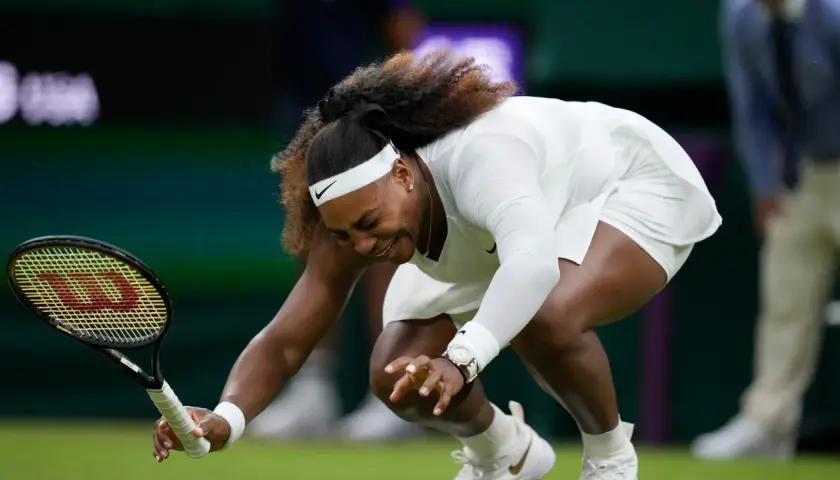 Serena Williams upada na kort podczas meczu tenisa w Wimbledonie, trzymając rakietę.