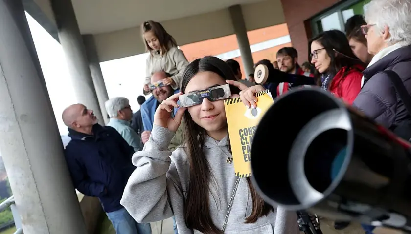 Joven mira un eclipse con gafas especiales, cerca de un telescopio con forma de lámpara cónica.