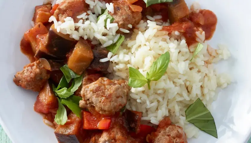 Herzhafte Salsiccia-Zubereitung in der Pfanne mit Auberginen, Paprika und Reis, garniert mit frischem Basilikum.