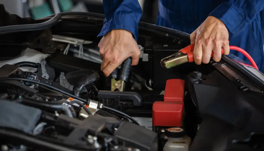Mekaniker kopplar startkablar för att ladda nytt bilbatteri.