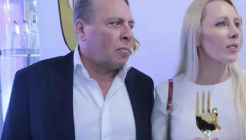 Wojtek Kurowski, wiek nieznany, w garniturze i białej koszuli, obok kobiety z złotym trofeum w kształcie dłoni.