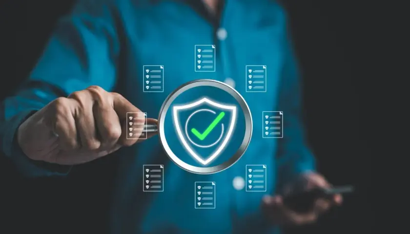 Un uomo esamina documenti con una lente d'ingrandimento, evidenziando un simbolo di scudo con un segno di spunta verde, a simboleggiare la sicurezza e l'efficienza nella sanità pubblica.