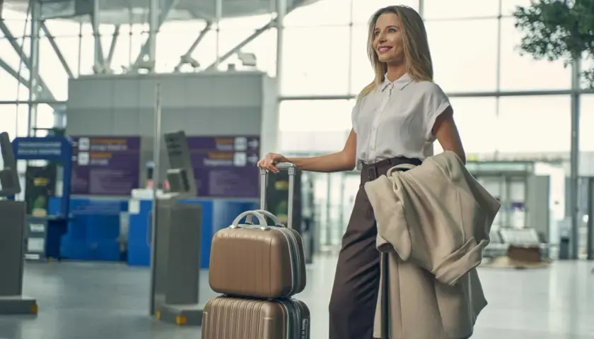 Elegancka kobieta w stylowym ubraniu do samolotu, z walizkami i płaszczem, czeka na lotnisku.