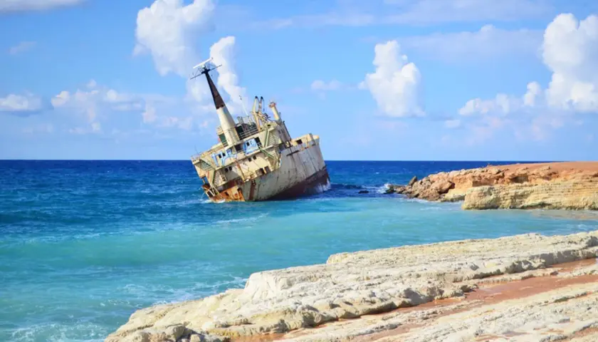 Wraki statków na pafos plażach. Zardzewiały statek osiadł na mieliźnie przy skalistym wybrzeżu, woda jest turkusowa, a niebo błękitne z białymi chmurami.