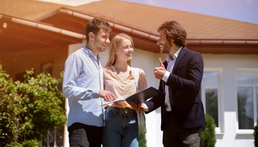 Un couple discute avec un agent immobilier devant une maison, signe d'une vente en cascade réussie.