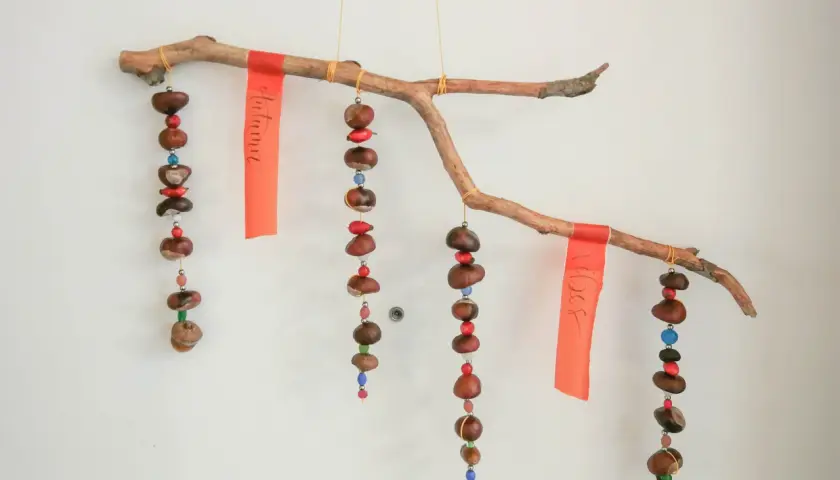 Ein schönes Herbst-Mobile zum Basteln mit Kindern: Kastanien, Beeren und bunte Perlen hängen an einem Ast.