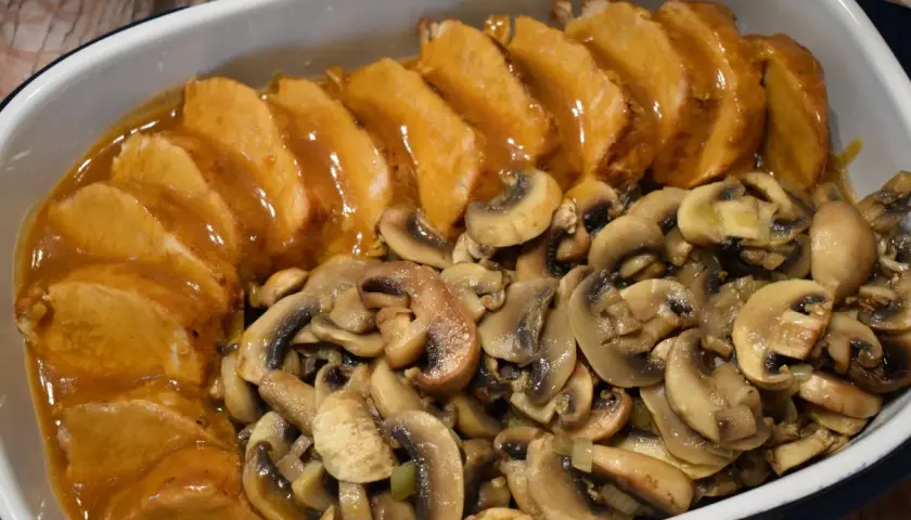 Pyszny schab z pieczarkami w sosie, podany w naczyniu żaroodpornym. Aromatyczne pieczarki idealnie komponują się z soczystym mięsem.