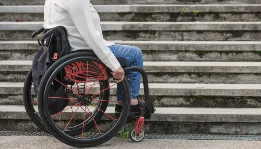 Osoba na wózku inwalidzkim, część grupy inwalidzkiej, siedzi przed kamiennymi schodami.