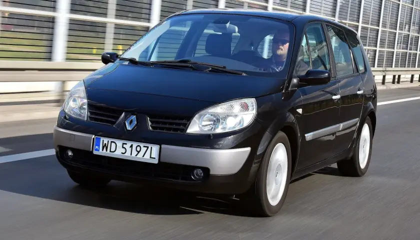 Czarny Renault Scenic 2 jedzie po drodze. Kierowca w okularach przeciwsłonecznych prowadzi auto.