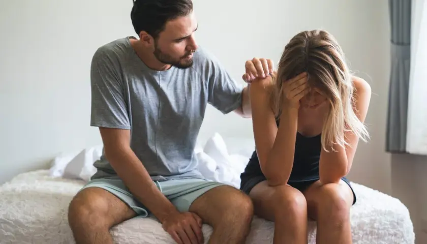 Hombre consuela a mujer afligida en la cama. ¿Qué significa soñar que tu pareja te es infiel?