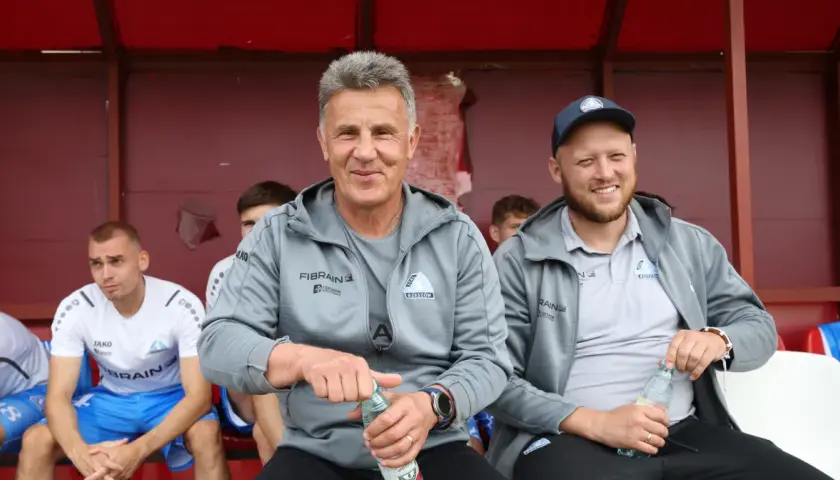 Marek Zub, trener Stali Rzeszów, z uśmiechem na twarzy, siedzi na ławce z butelką wody.