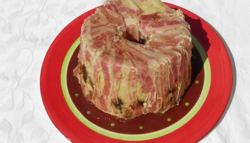 Un pâté en croûte de lard, une recette qui ne demande pas de farcement. Il est servi sur une assiette rouge décorée.